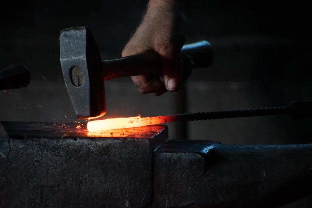 Blacksmith hammering a red-hot steel bar on an anvil